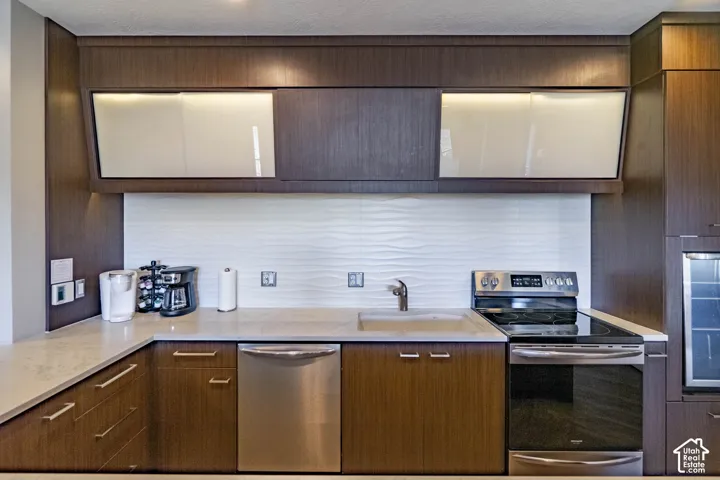 Modern kitchen featuring dark wood-finish cabinetry, light stone countertops, and a textured white tile backsplash