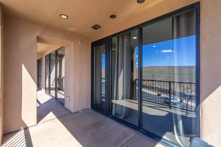 Spacious balcony featuring stucco walls, multiple glass sliding doors, recessed lighting, and a black wrought iron railing