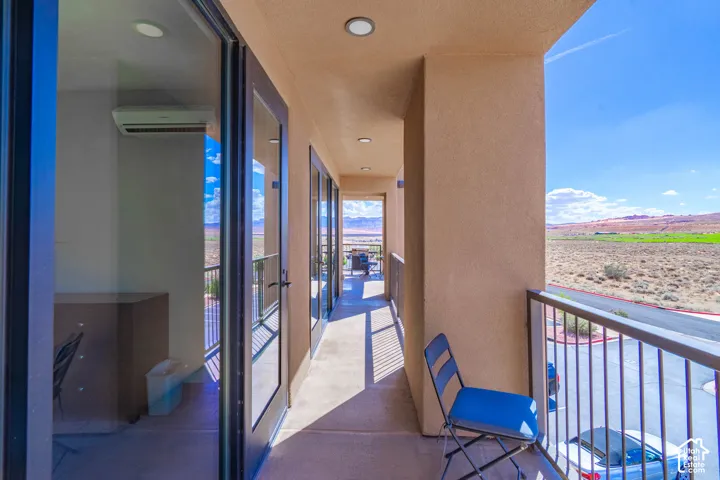 Exterior balcony with beige stucco facade, multiple glass-paned doors, recessed lighting, and a metal railing