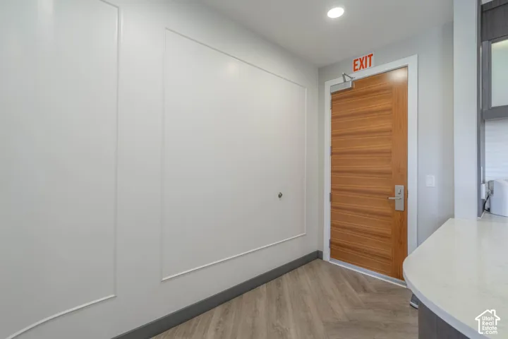 Wood-grain door with brushed metal hardware, recessed lighting, and chevron-patterned wood-finish flooring