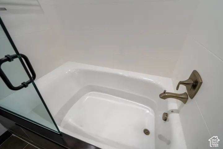 White bathtub with bronze-finish fixtures, white tile surround, and a clear glass shower enclosure with dark framing