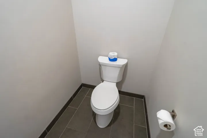 White commode with a ceramic tank and bowl, tile flooring, and a wall-mounted toilet paper holder