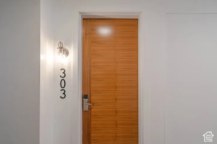 Wood-finish entry door with a digital lockset, brushed nickel sconce, and modern house numbers