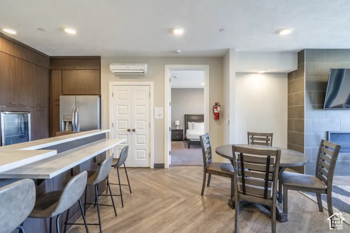 Open-concept common area featuring wood-finish flooring, a built-in kitchen island, stainless steel refrigerator, and tiled fireplace surround