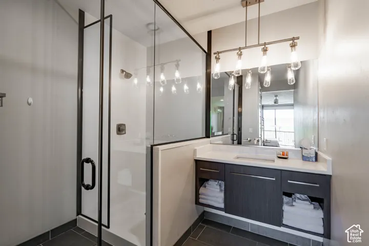 Glass-enclosed shower with dark-framed door, floating vanity with integrated sink, rectangular mirror, and linear pendant lighting fixture
