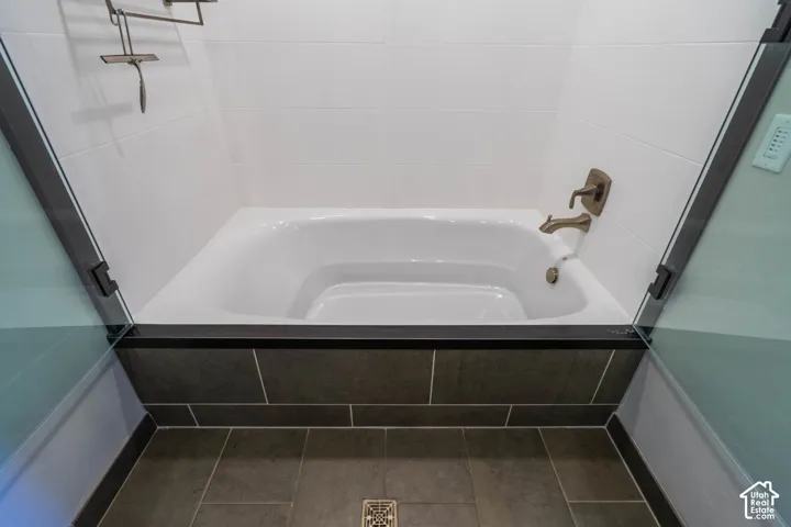Soaking tub with bronze fixtures, framed by clear glass panels, white subway tile walls, and dark large-format floor tiles