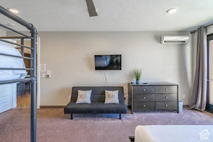 Plush carpet flooring, ceiling fan, recessed lighting, wall-mounted air conditioning unit, and private exterior access