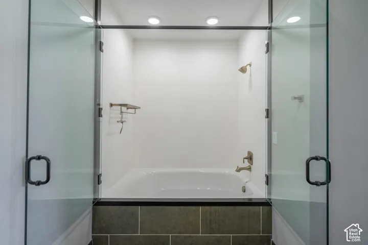 Bathtub with a glass enclosure, white subway tile surround, dark tile wainscoting, and recessed lighting