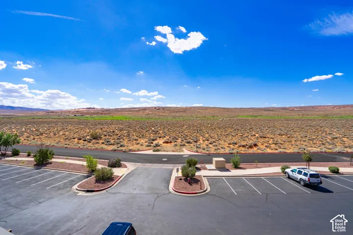 Paved parking area with marked spaces and landscape islands, bordered by desert terrain and distant geological formations