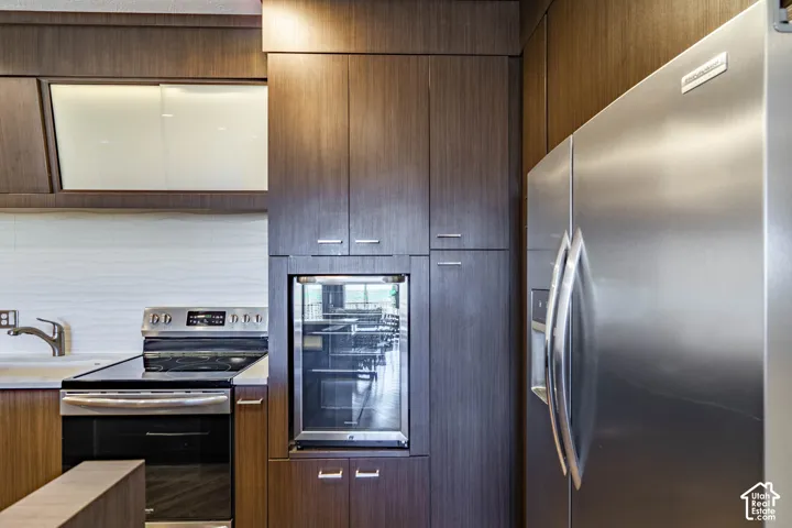 Stainless steel appliances, wood-finish cabinetry, white subway tile backsplash, under-cabinet lighting, and a built-in beverage refrigerator