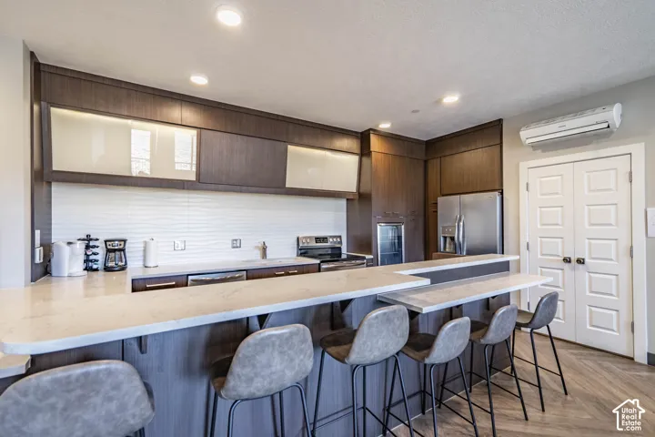 Kitchen featuring wood-finish cabinetry, stainless steel appliances, white tile backsplash, and a breakfast bar with stone countertops