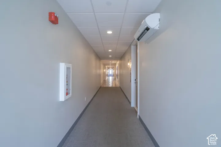 Recessed lighting, drop ceiling, wall-mounted air conditioning unit, gray carpet flooring, and light gray wall paint