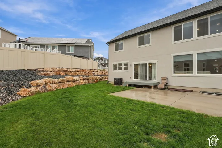 Expansive backyard with a manicured lawn, a multi-tiered rock retaining wall, and a concrete patio