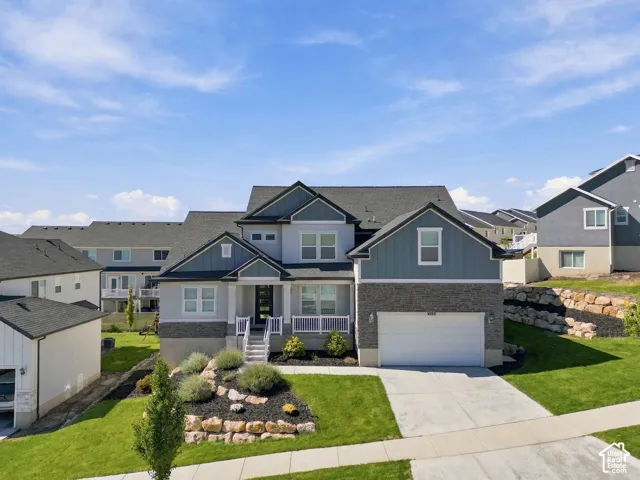 Two-story residence featuring a gray and blue exterior, an attached garage, a front porch with white railings, and a landscaped rock garden