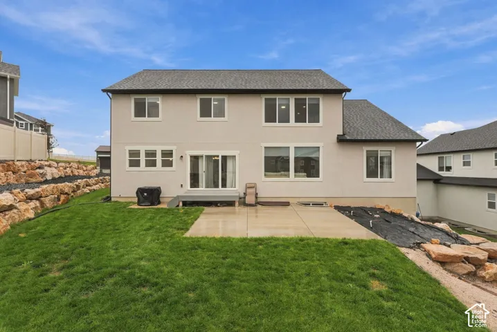 Rear exterior with a concrete patio, sliding glass door, and a tiered rock retaining wall