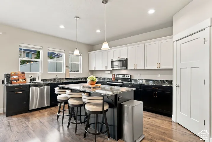 Kitchen featuring wood-finish flooring, two-tone cabinetry, stainless steel appliances, a center island with pendant lighting, and recessed ceiling lights