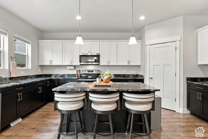 Two-tone cabinetry with contrasting finishes, dark countertops, stainless steel appliances, central island with seating, and laminate flooring