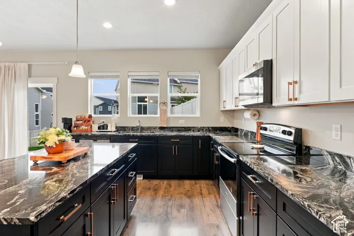 Kitchen featuring two-tone cabinetry with contrasting hardware, black countertops, stainless steel appliances, and laminate flooring