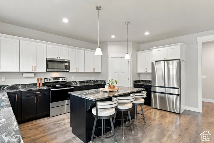 Gourmet kitchen featuring white upper cabinetry, dark lower cabinetry, stainless steel appliances, a center island with pendant lighting, and laminate flooring