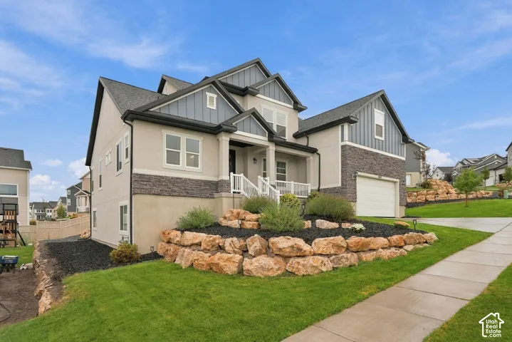 Contemporary residence featuring a stucco and stone facade, gabled rooflines, an attached garage, and a landscaped rock wall with shrubbery