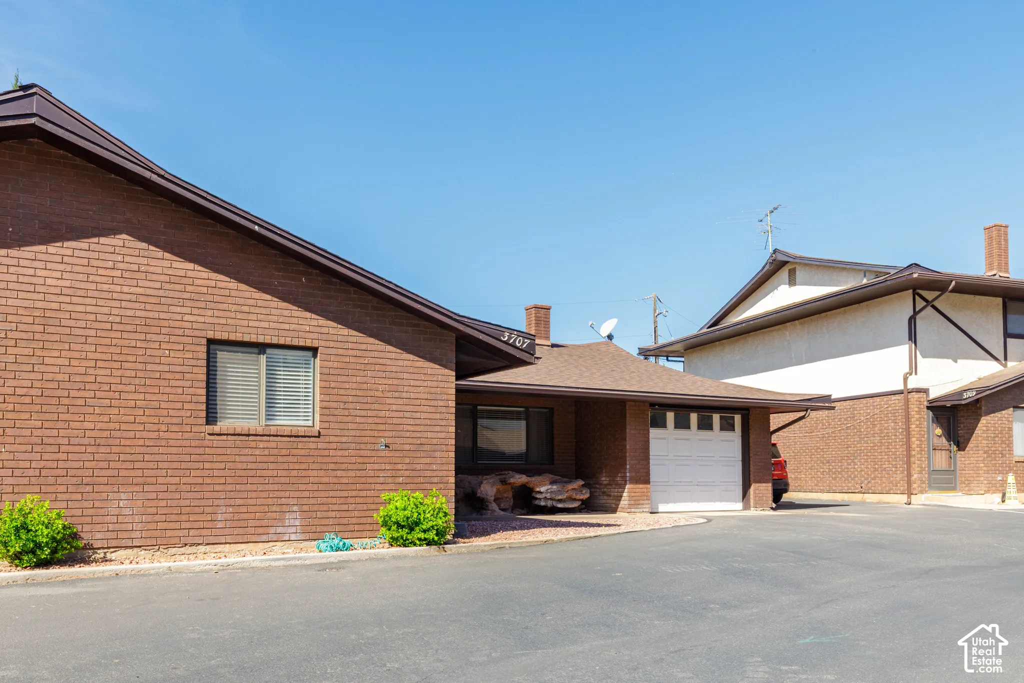 Brick exterior with a peaked roofline, attached garage with white door, and foundational plantings