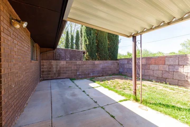 Covered patio space with concrete flooring, brick exterior wall, and metal support posts