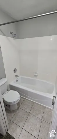 White tub and shower combination with chrome fixtures, tiled flooring, and a white toilet