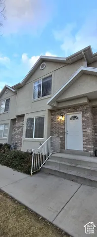 Textured stucco exterior with brick accents, multi-pane windows, front entry with transom window, and concrete steps with handrail