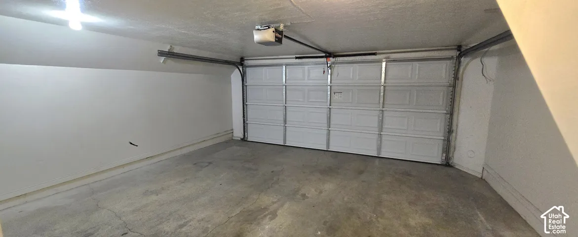 Attached single-bay garage featuring a concrete floor, white panel garage door, and an overhead garage door opener