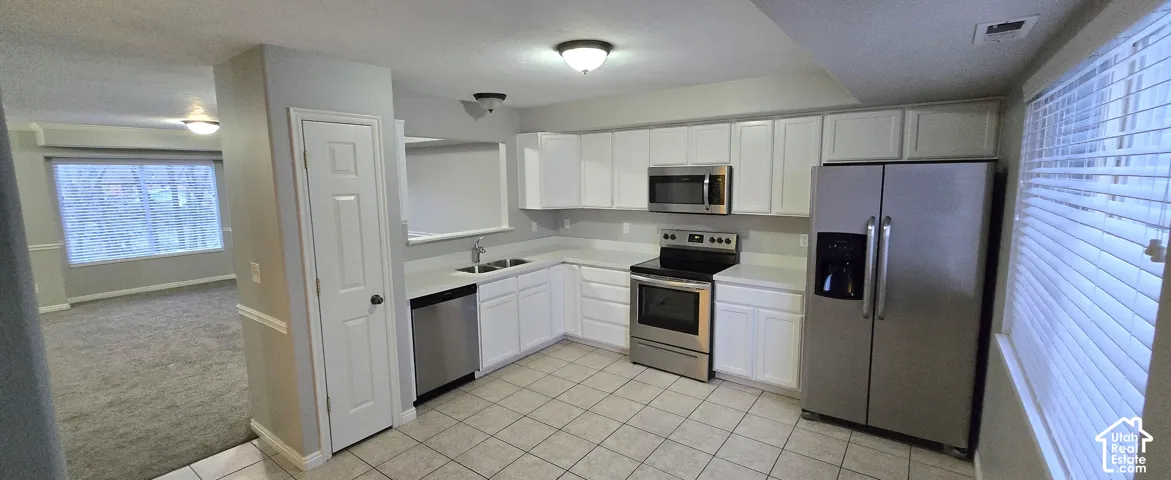 Kitchen featuring white cabinetry, stainless steel appliances, a corner sink, tiled flooring, and a window with blinds