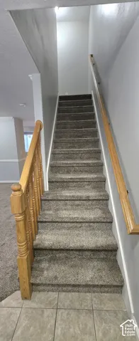Carpeted staircase with wooden handrails and balusters, featuring a tile landing