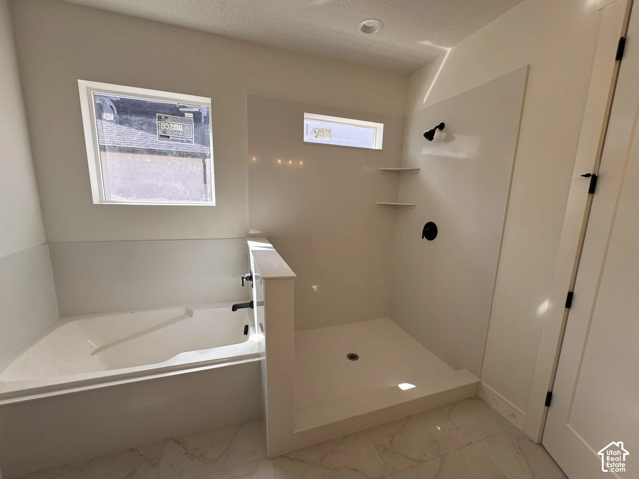 Recessed lighting, large soaking tub, walk-in shower with built-in shelving, matte black fixtures, and light-toned tile flooring