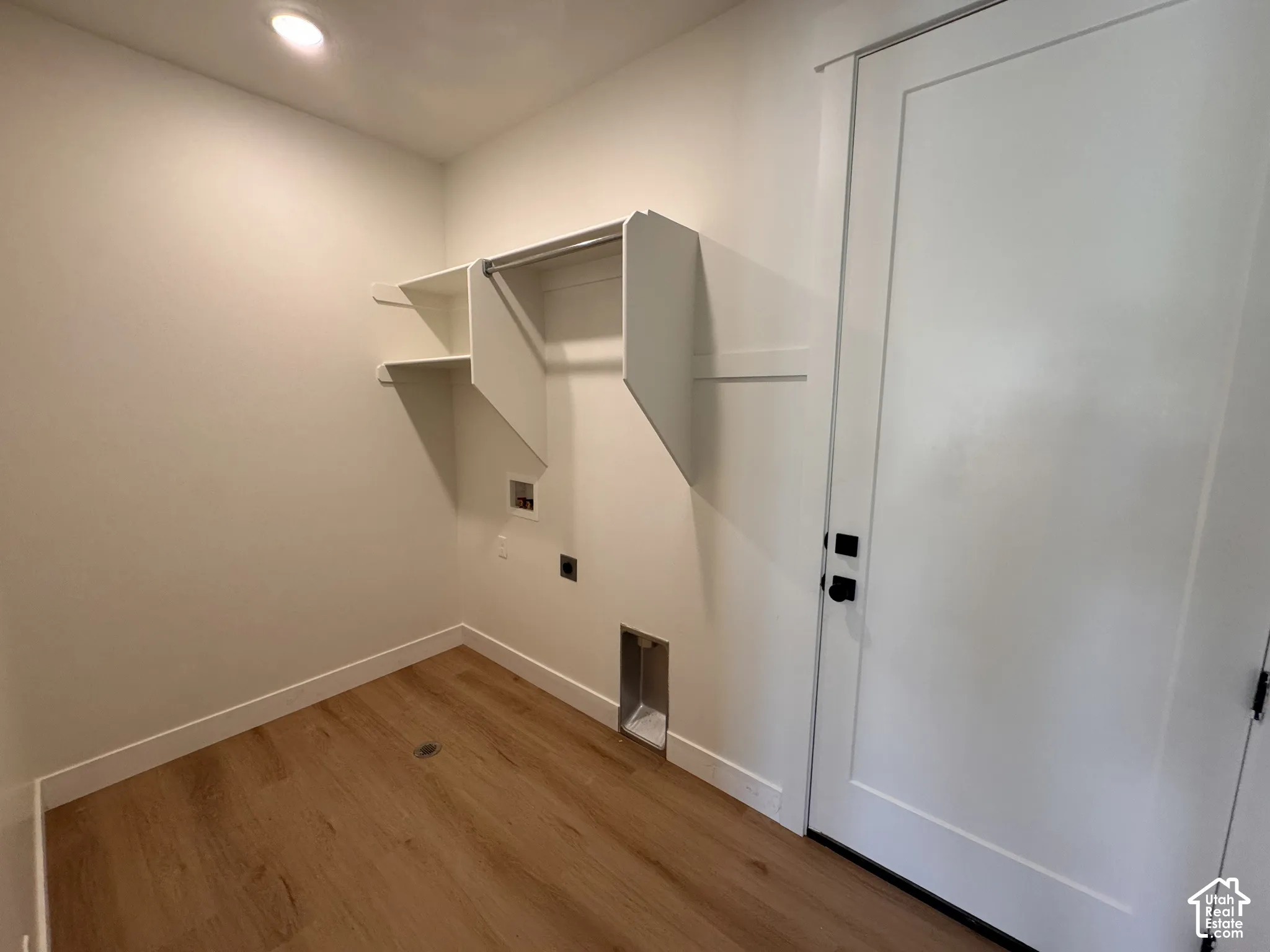 Recessed ceiling lighting, wood-finish flooring, white walls, built-in shelving, and a flat-panel door with black hardware