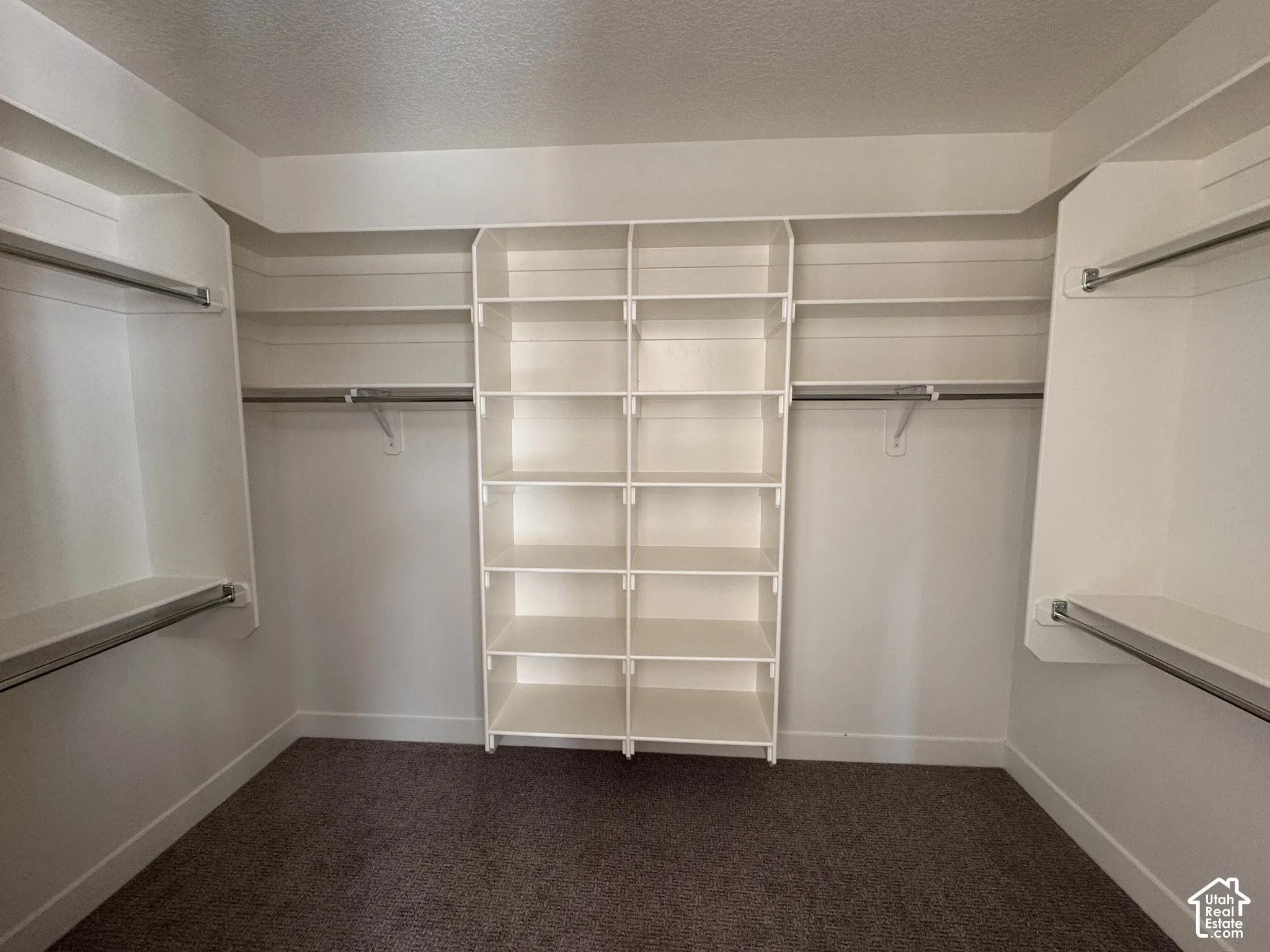 Spacious walk-in closet featuring custom white shelving with multiple compartments for organized storage, dual clothing rods on either side, and neutral carpeting throughout