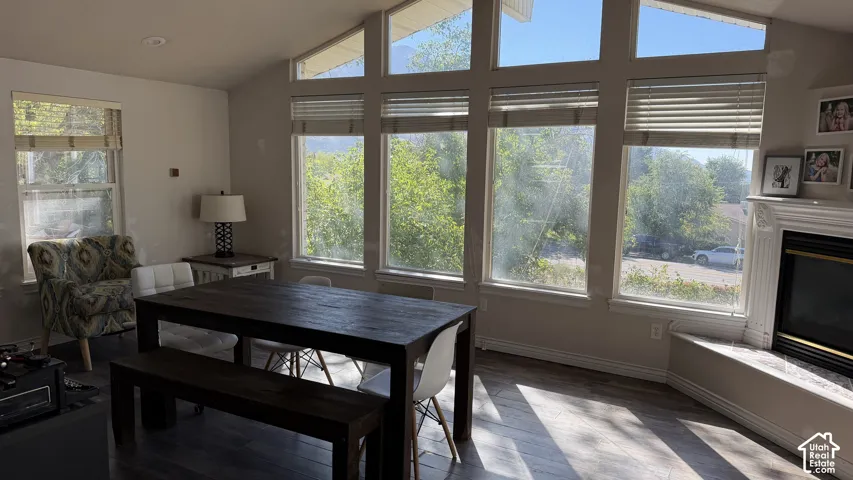Vaulted ceiling room with multiple large windows, wood-finish flooring, and a built-in fireplace featuring a decorative mantel