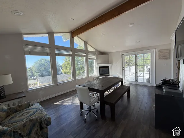 Vaulted ceiling with exposed wood beam, recessed lighting, wood-finish flooring, corner fireplace with white mantel, and sliding glass doors to exterior