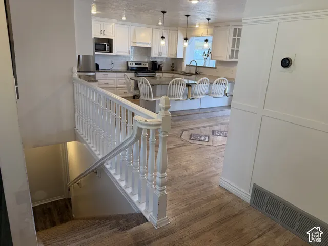 White shaker cabinetry, stainless steel appliances, wood-finish flooring, white paneling, and an open-concept kitchen
