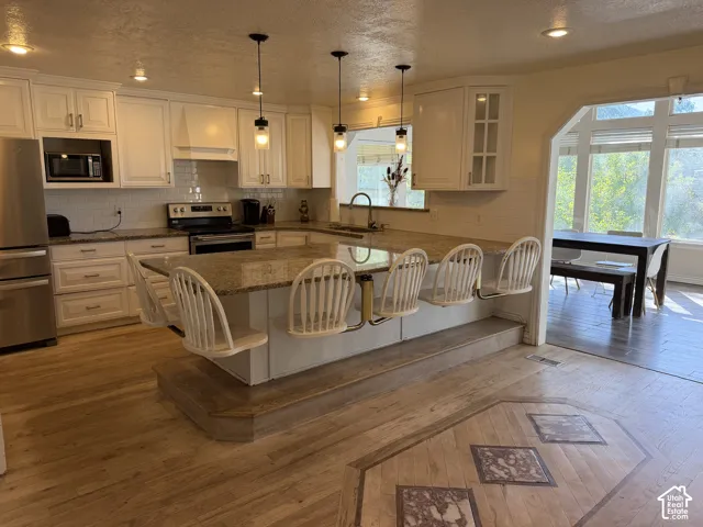 Kitchen featuring white cabinetry, stainless steel appliances, a granite countertop island with seating, a white subway tile backsplash, and light wood-finish flooring