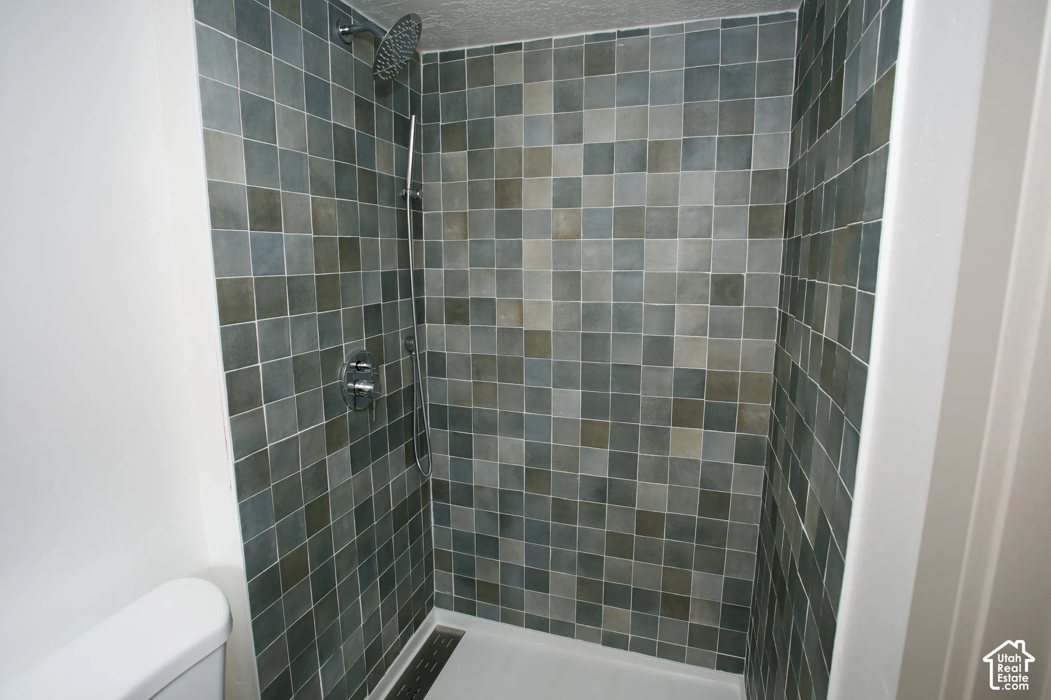 Tiled shower with a rainfall showerhead, handheld shower fixture, and a linear drain