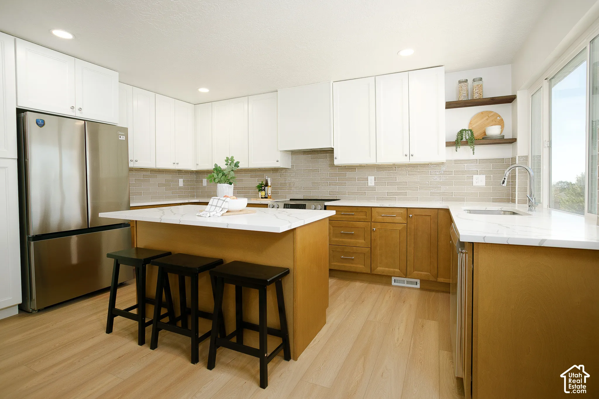 Kitchen featuring wood-finish flooring, a two-tone cabinetry scheme, stainless steel appliances, a tile backsplash, and an island with a light-toned countertop