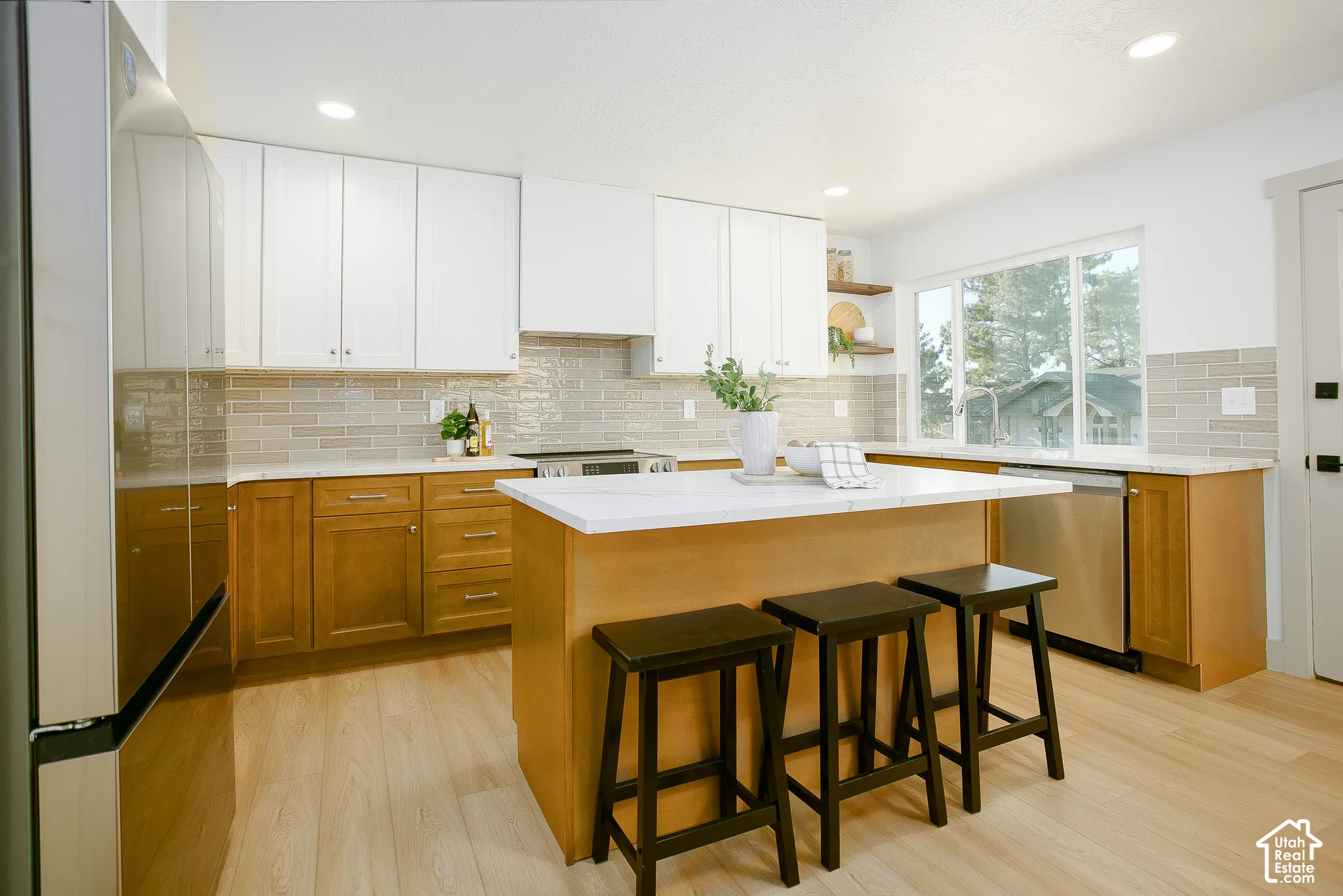 Kitchen featuring light wood-finish flooring, two-tone cabinetry, a central island with a white countertop, stainless steel appliances, and a tiled backsplash