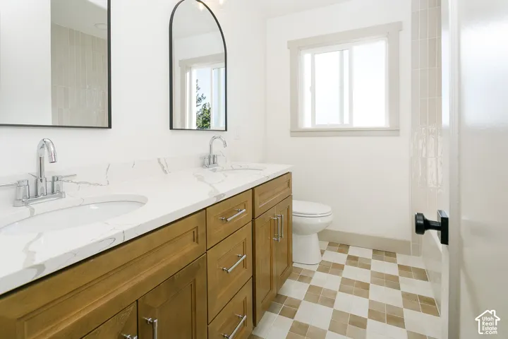 Dual vanity with integrated sinks, white countertop, wood-finish cabinetry, and checkerboard floor tiling