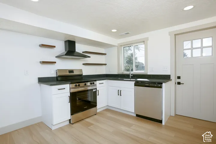 Kitchen featuring white cabinetry, dark countertops, stainless steel appliances, and wood-finish flooring