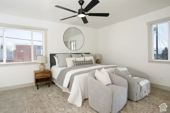 White walls with light gray trim, two large windows, black ceiling fan with integrated lighting, and neutral carpeting