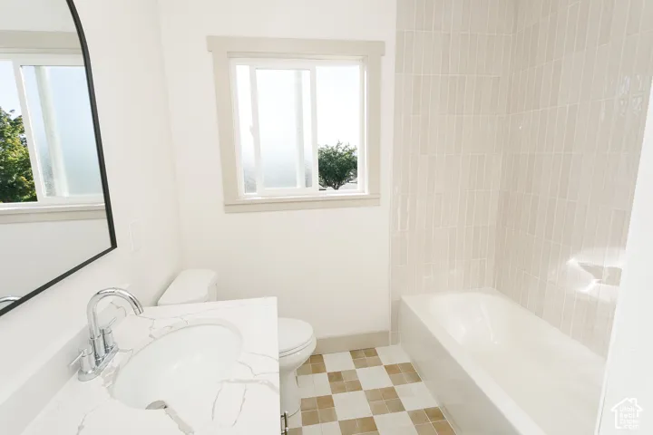 White vanity with integrated sink and chrome faucet, checkered tile flooring, white bathtub with vertical tile surround, and an arched mirror