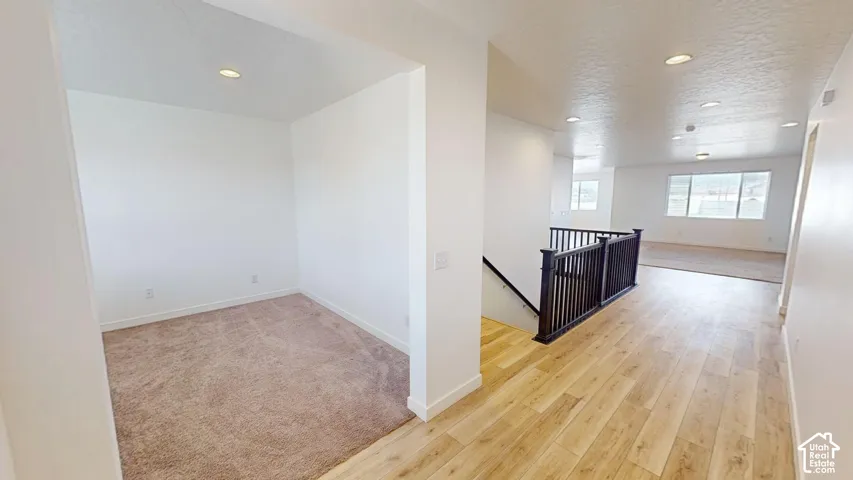 Open-concept interior featuring wood-finish flooring, recessed lighting, and a dark wood-finish staircase railing