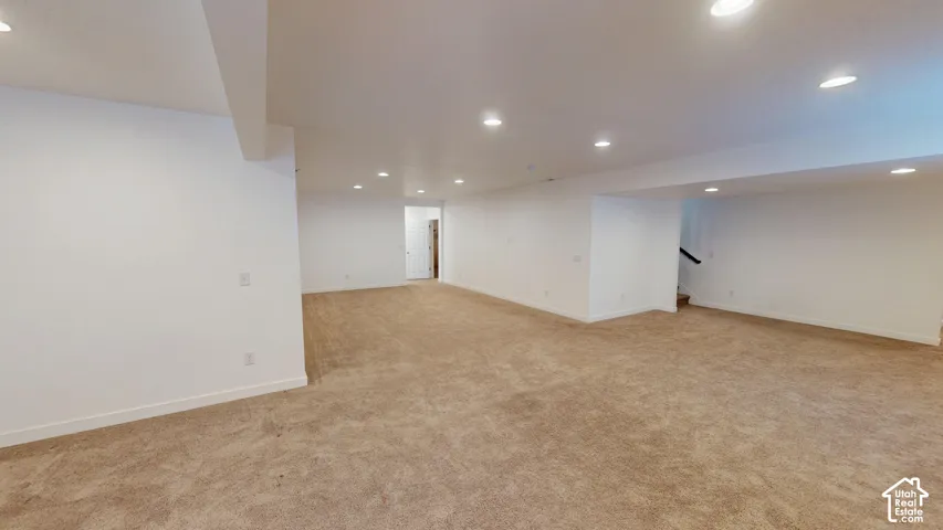 Expansive open-concept room featuring warm-toned carpeting, recessed lighting, and crisp white walls