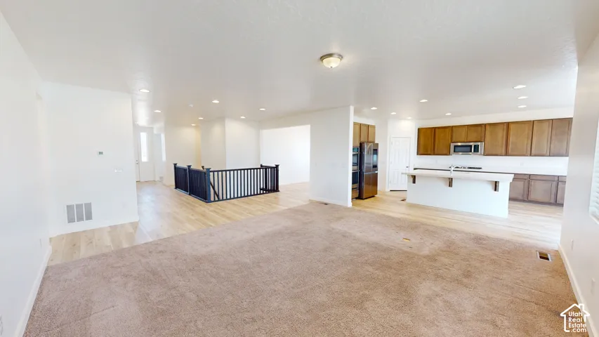 Open-concept living area featuring wood-finish flooring, recessed lighting, and a kitchen with wood cabinetry and stainless steel appliances