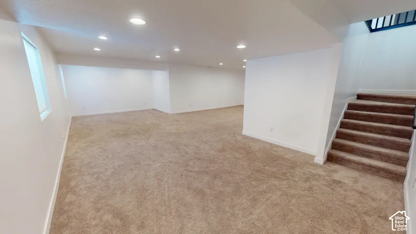 Expansive open-concept room with recessed lighting, light-toned carpeting, and a full staircase with dark-finished railings