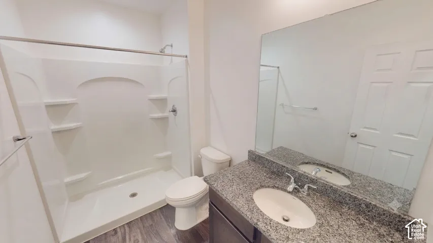 Shower with built-in shelving, wood-finish flooring, toilet, vanity with dual undermount sinks, and a large mirror